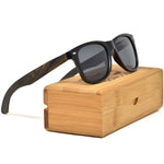 Load image into Gallery viewer, A pair of ebony wood sunglasses with black polarized lenses resting on a bamboo storage box.
