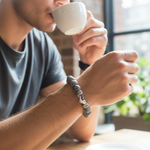 Load image into Gallery viewer, Man wearing a Genuine Grey Jasper Bracelet. This 8.5" masterpiece features 10mm natural stone beads accented by industrial-grade 316L stainless steel and clasp closure. It’s more than an accessory—it’s a symbol of balance and resilience for the modern man
