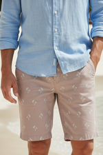 Load image into Gallery viewer, Our Model is  wearing a light blue shirt and with our Soul of London pink bermuda shorts with a subtle palm tree pattern on a beach.
