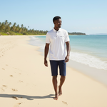 Load image into Gallery viewer, Our model is wearing a white Cotton with blue and white floral trim on the false pocket, with blue shorts walking on a sandy beach
