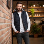 Load image into Gallery viewer, Man wearing a navy puffer vest with removable hood  in an indoor setting with shelves and plants.

